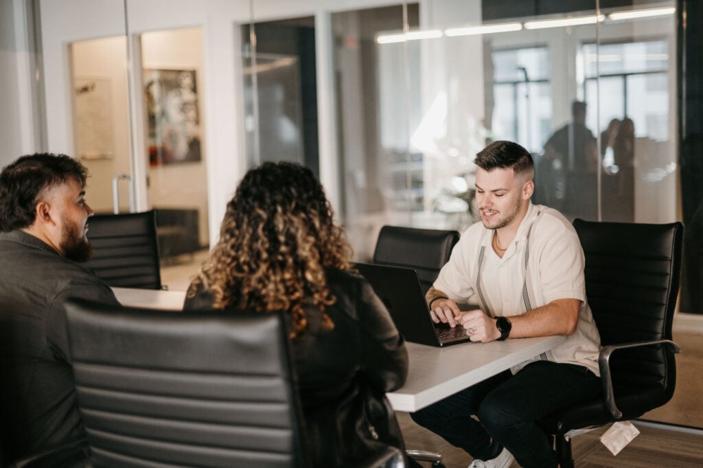 Hook Agency team collaborates at a modern conference table, reviewing website elements. Glass walls and large windows in background.