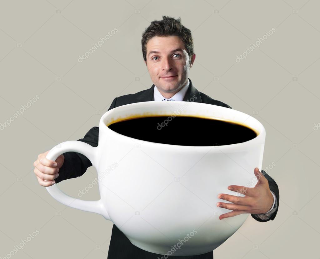 A man in a suit smiling while holding an oversized coffee cup filled with black coffee, this quirky stock photo fits perfectly for anyone searching through stock images or crafting clever memes against a plain backdrop.