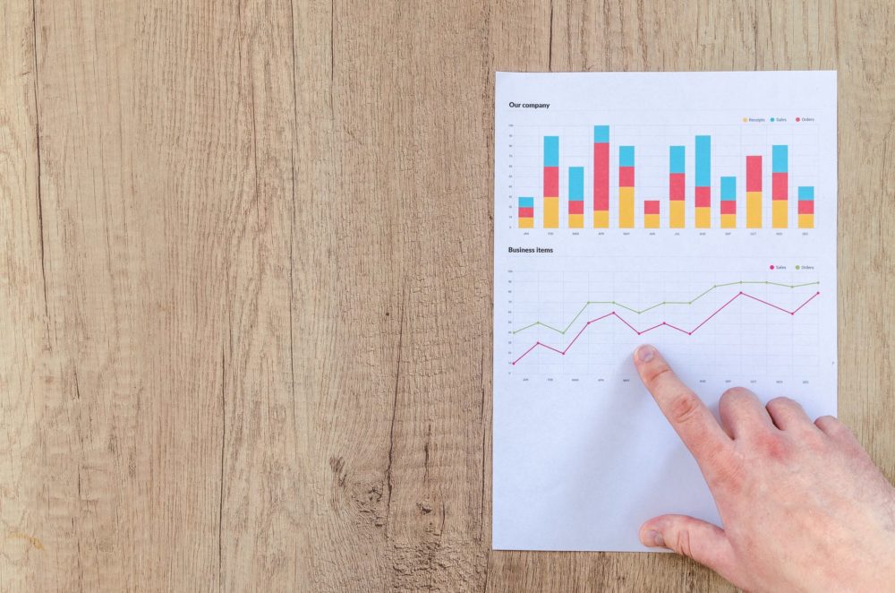 A hand points to a line graph on paper atop a wooden surface, accentuated by a vivid bar chart illustrating top lead generation trends. These graphs, with their colorful lines and bars, offer key insights for optimizing lead generation strategies.