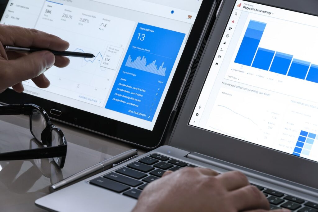 Two team members review SEO charts on tablet and laptop; one highlights data with a pen. Glasses sit on the Hook Agency desk.