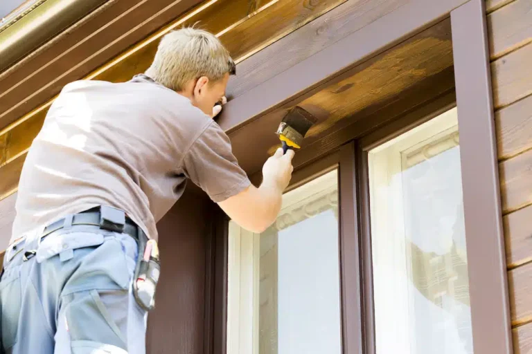 A skilled craftsman meticulously paints a window frame, demonstrating the mastery and precision akin to an artist in marketing. Armed with a brush and tool belt, he concentrates intently on his wooden canvas.