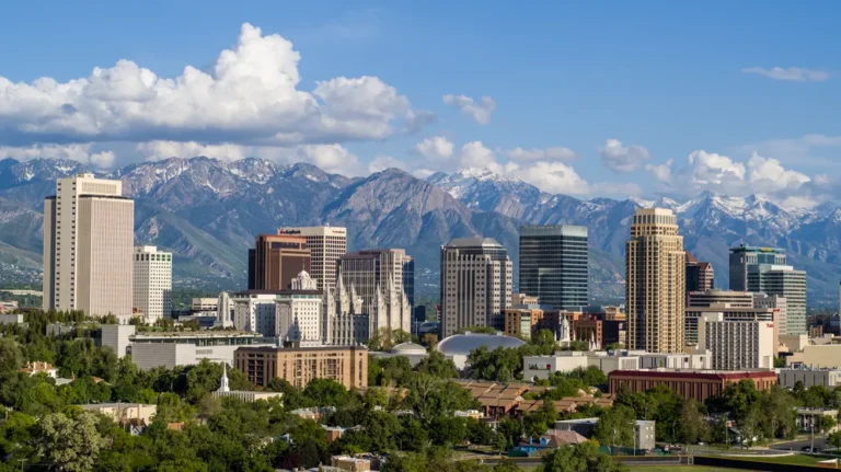Experience the Salt Lake City skyline, where modern skyscrapers rise beside historic architecture against a backdrop of snow-capped mountains. This picturesque scene, under a blue sky dotted with clouds and framed by lush greenery, embodies the seamless blend of tradition and innovation found in our cutting-edge web design at Hook Agency.