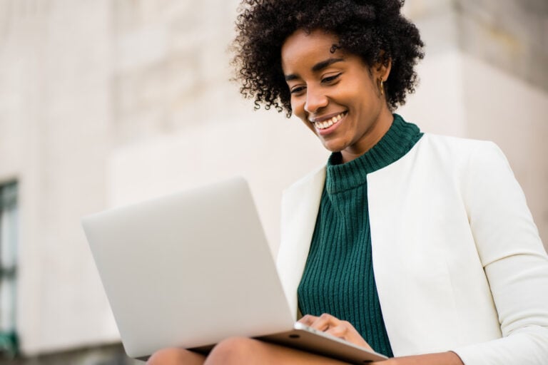 Hook Agency's website features an image of a smiling individual with curly hair outdoors in Boston, dressed in a green top and white jacket, working on a laptop against a blurred backdrop of a light-colored brick wall.