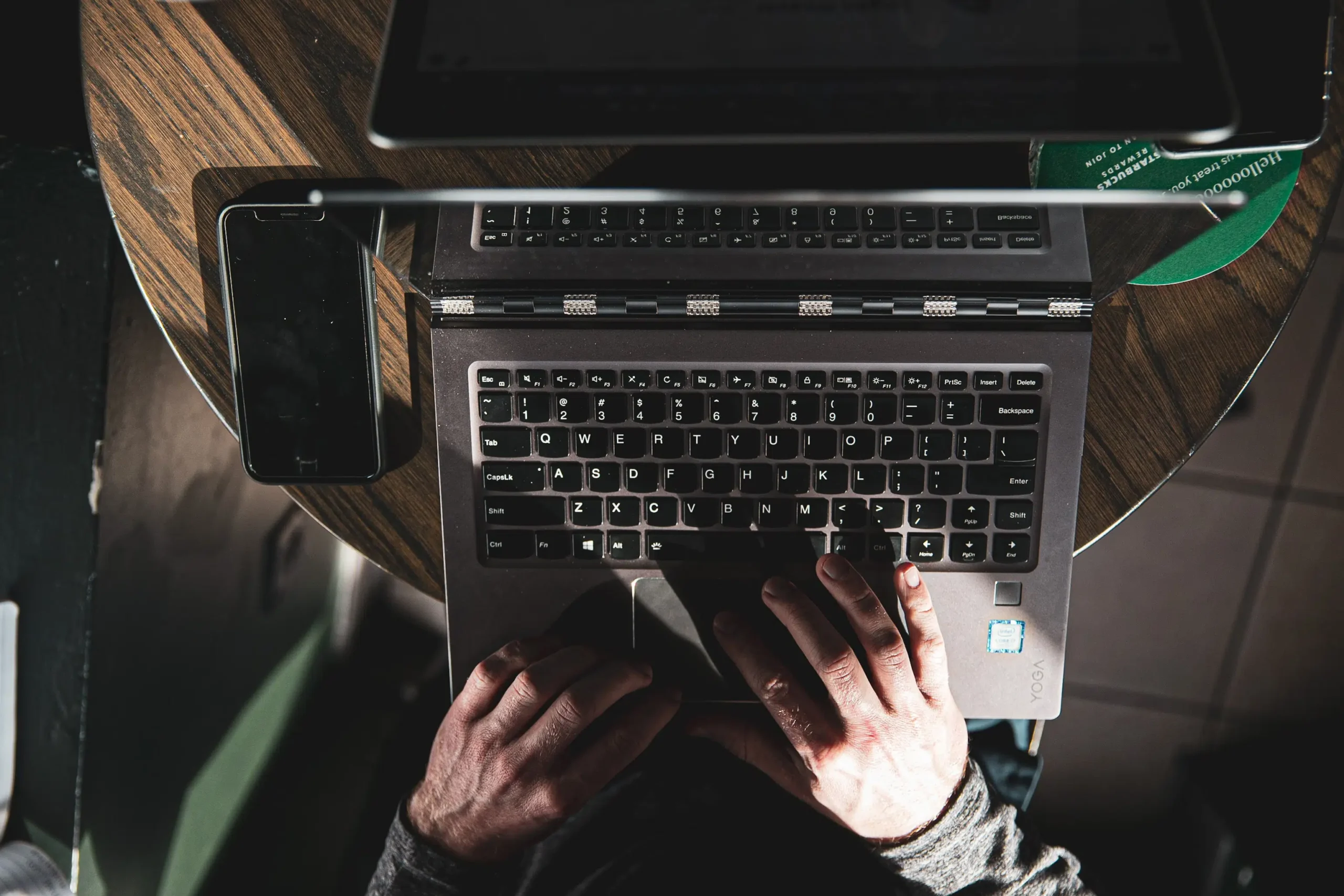 Overhead view of an individual typing on a laptop at a wooden table, with a smartphone to the left showing Mankato SEO results amidst dim lighting for a focused, intimate ambiance.