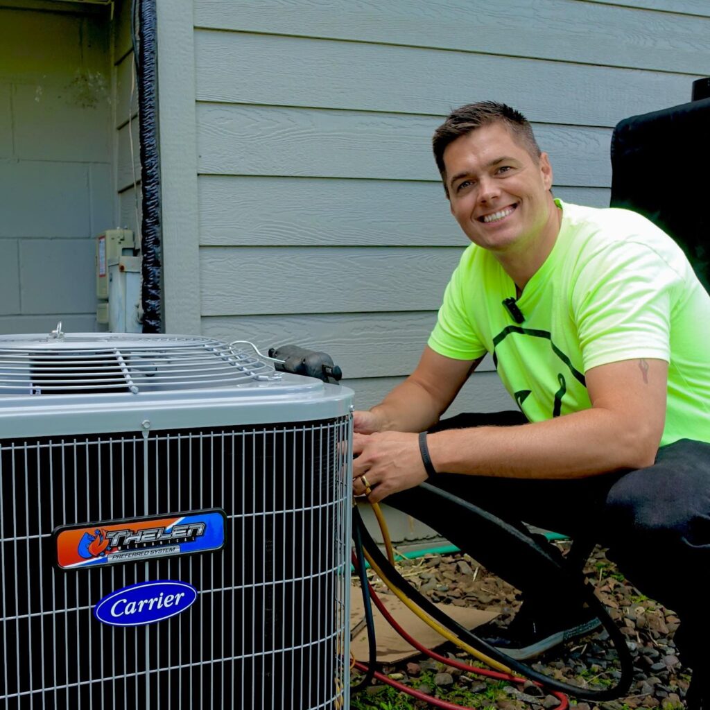 A person in a bright yellow T-shirt crouches next to a Carrier air conditioning unit, symbolizing the promising outlook for HVAC industry statistics in 2024 and 2025. With short hair and a confident smile, they are framed against the modern gray siding of a house.