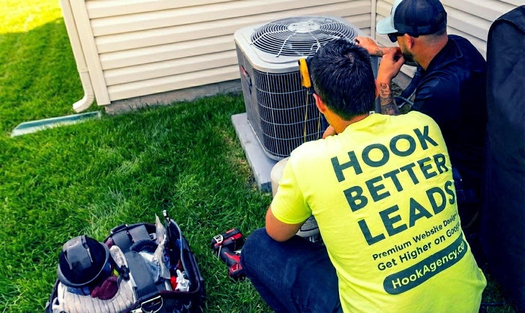 Home Services marketing and lead generation Hook Agency Two men repair an AC unit by a house; one wears a "HOOK BETTER LEADS" shirt, emphasizing effective HVAC marketing.