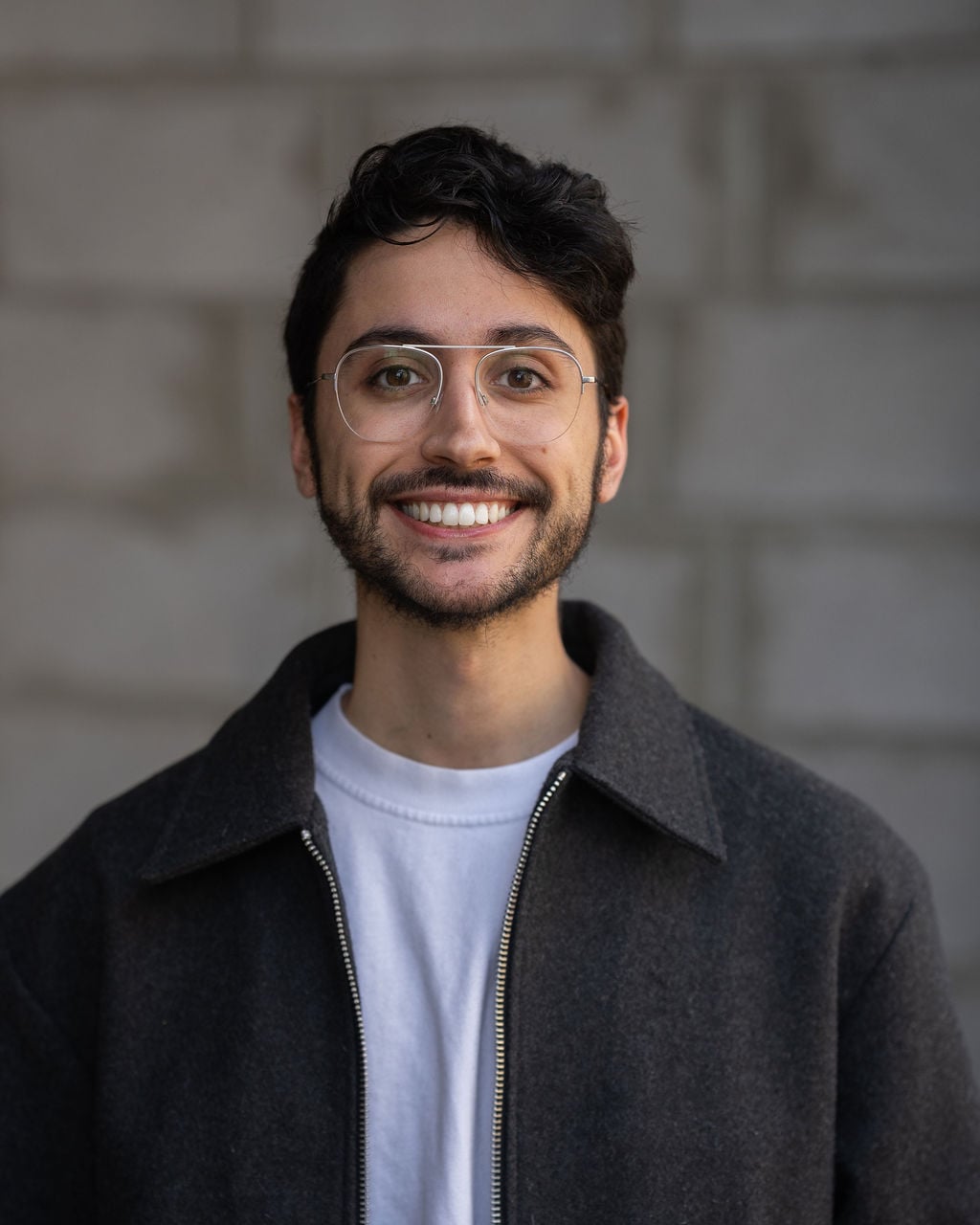Professional team member with short dark hair, glasses, and beard; photographed against a blurred gray background for Hook Agency.