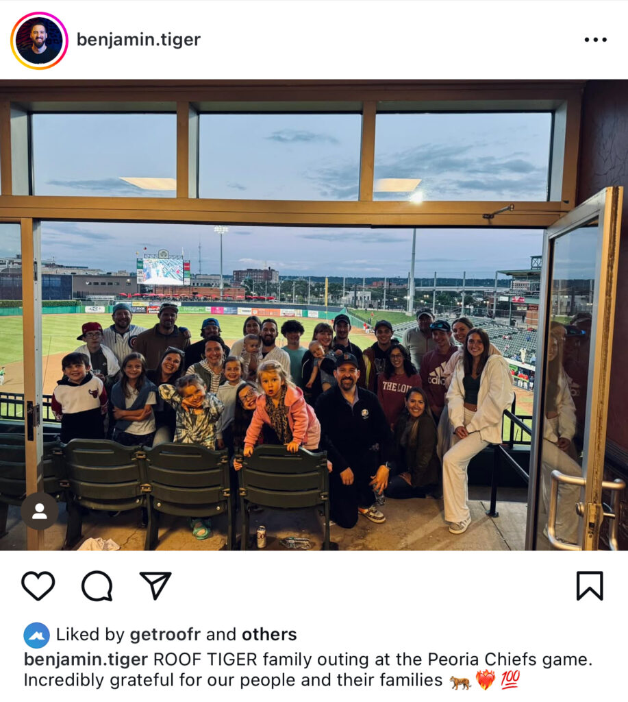 Team members of all ages gather in a stadium suite overlooking the Peoria Chiefs baseball field to celebrate National Roofing Week. Against a backdrop of city buildings and cloudy skies, the group showcases Hook Agency’s commitment to team spirit and industry pride.