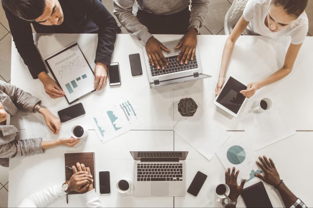 Top-down view of a diverse team at Hook Agency strategizing contractor marketing with laptops, charts, and coffee cups at the table.