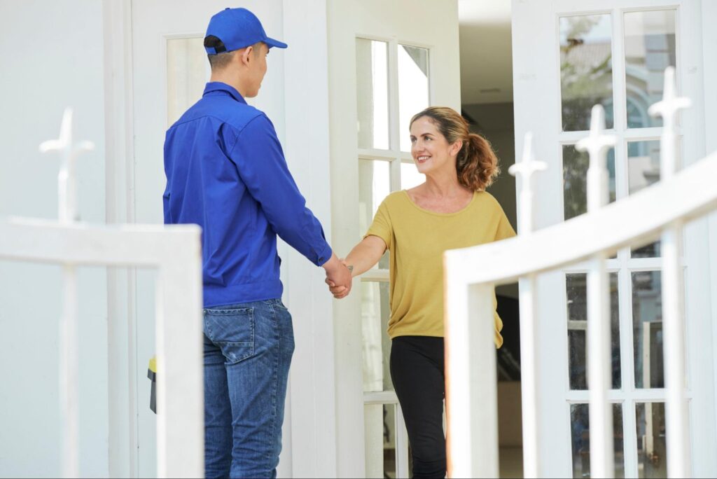 A woman greets an SEO expert at her door, shaking hands as they prepare to discuss revenue growth strategies for her business.