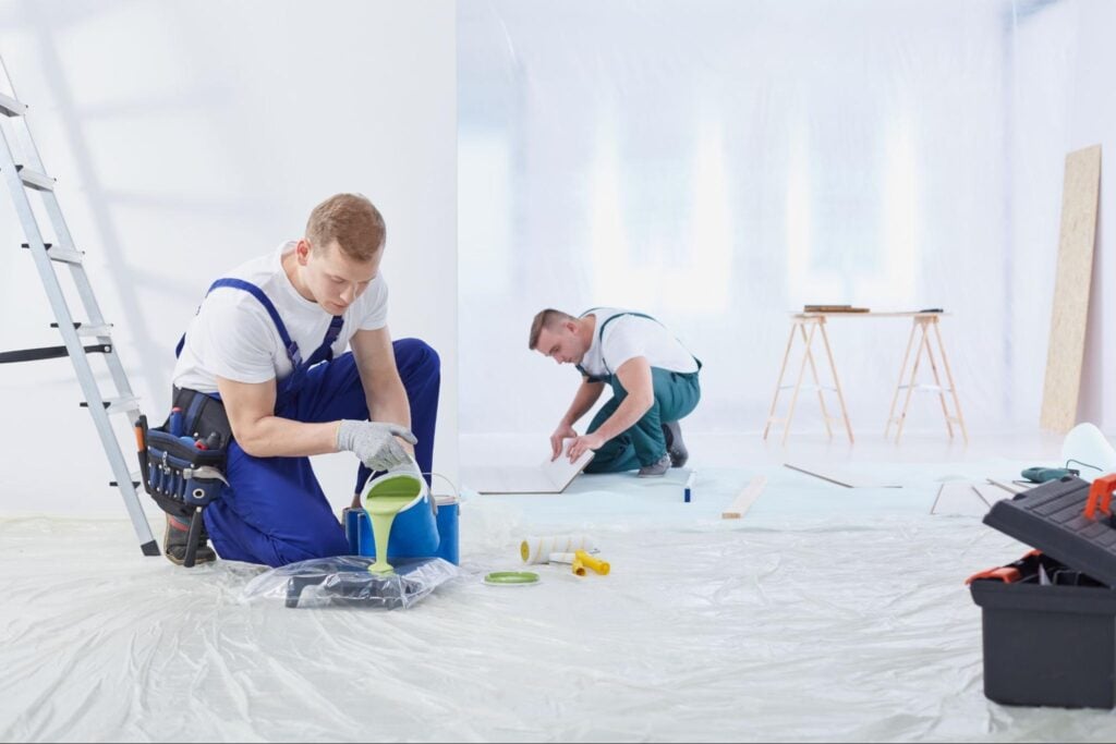 Two painters prepping a bright room—one pouring green paint, one measuring; tools and supplies visible, suited for lead generation.