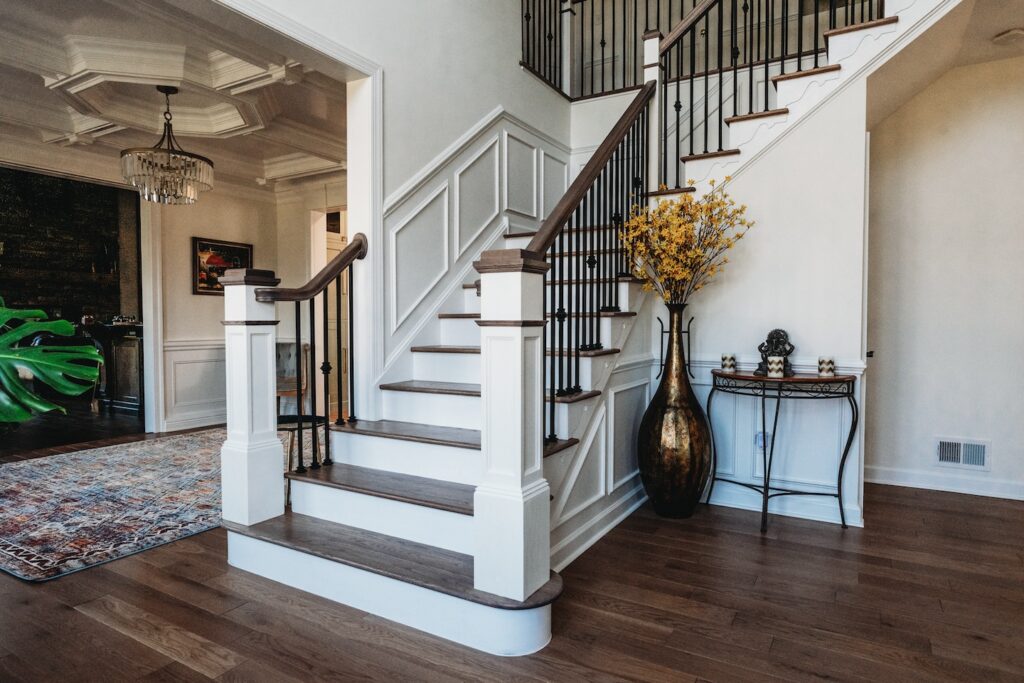 Modern, bright foyer with wood stairs, white paneling, ornate side table, yellow flowers—ideal remodeler marketing inspiration.