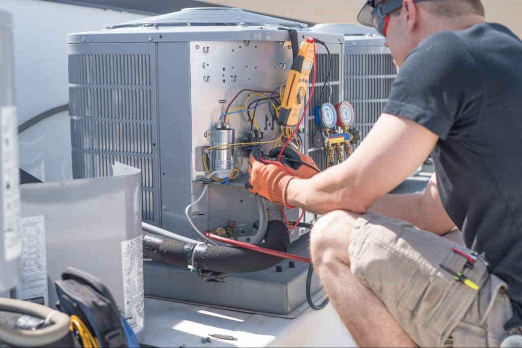 HVAC technician with safety gear repairs outdoor AC unit, testing wiring and components during routine service.