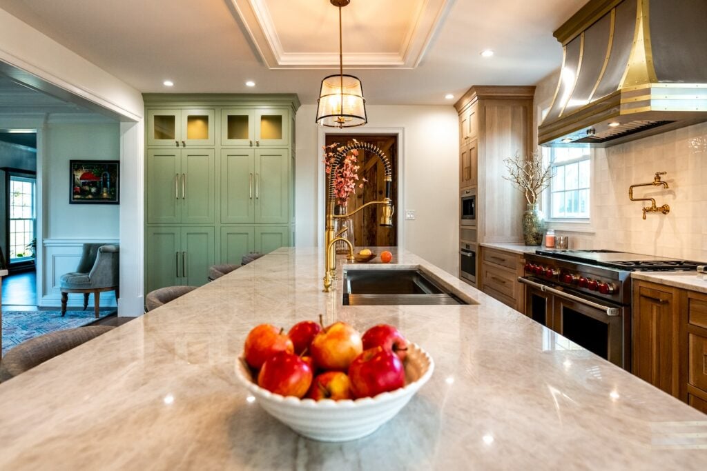 Showcasing a bright kitchen with marble island, gold faucet, green cabinets, brass hood stove—ideal for remodeler marketing inspiration.