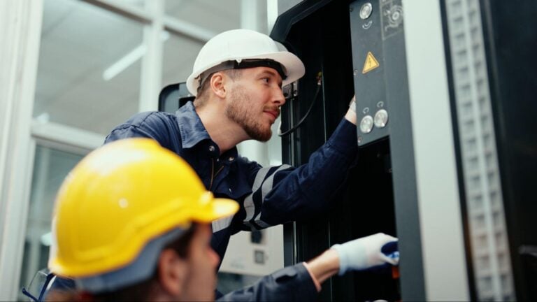 Two workers in safety helmets and gloves inspect industrial electrical equipment—showcasing expertise for electrician PPC marketing.