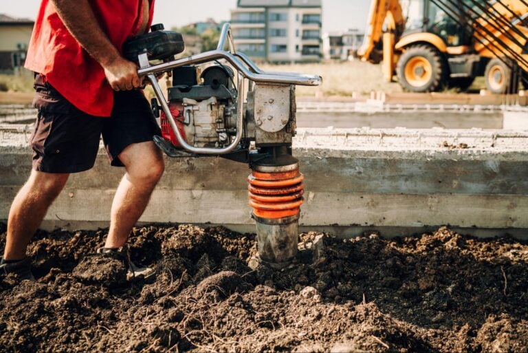 Construction worker compacts soil at a site with concrete foundation—ideal for showcasing top Foundation Repair SEO strategies.