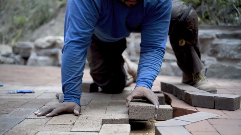 Professional hardscaper in blue shirt and brown pants installs bricks on pathway—ideal for U.S. hardscaping lead generation.