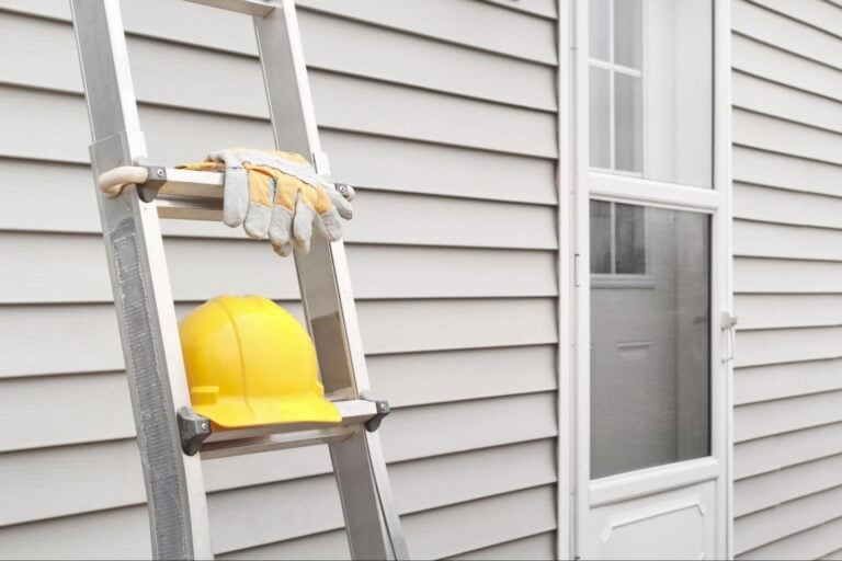 Yellow hard hat and gloves on a ladder against gray siding near a white-framed door—quality work Siding PPC can showcase.