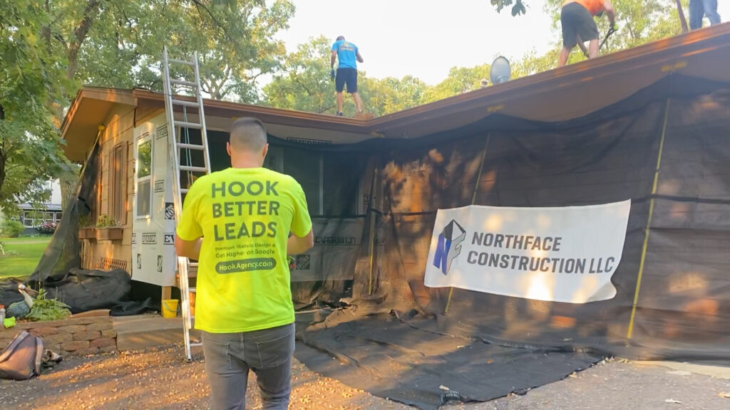 Worker in HOOK BETTER LEADS shirt observes roof installation; NORTHFACE CONSTRUCTION LLC banner promotes new roofing website.