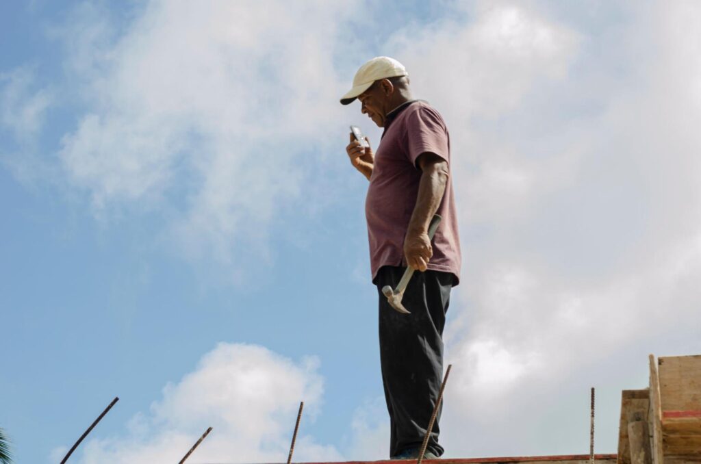 On a construction site, a man in a cap holds a hammer and phones his marketing partner to coordinate project plans for Hook Agency.