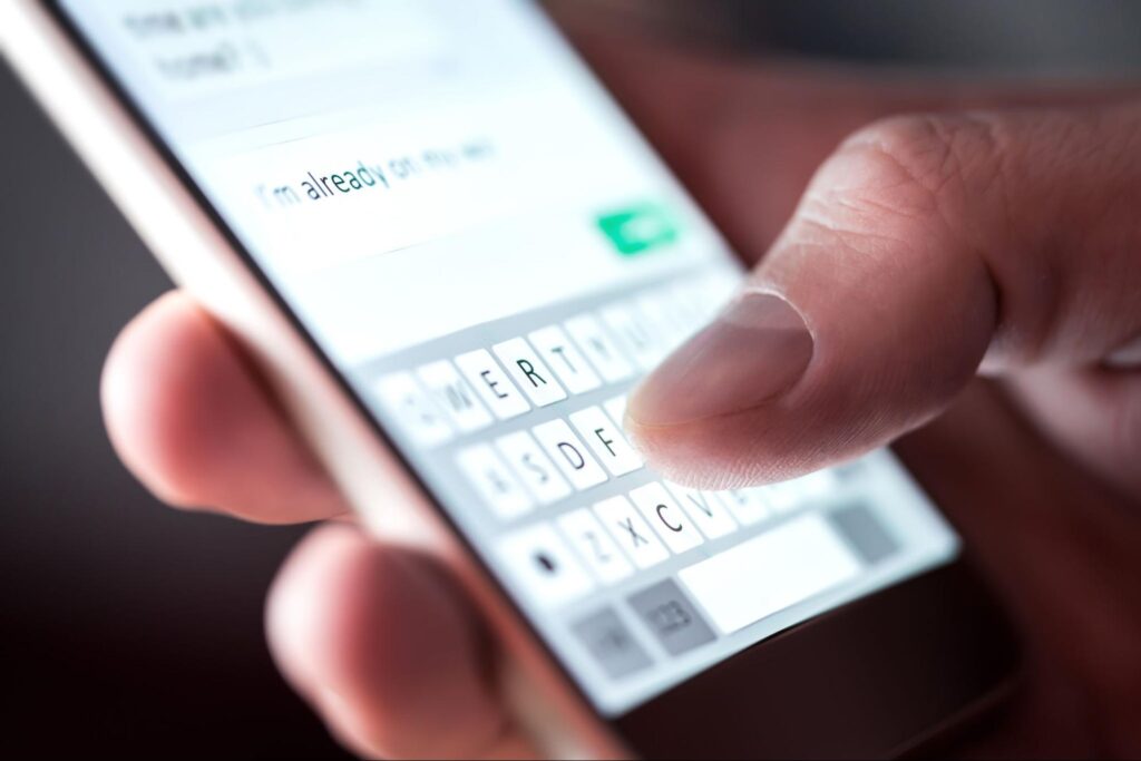 Close-up of a hand typing on a smartphone keyboard, composing a message for Omnipresent Marketing on Hook Agency’s website.