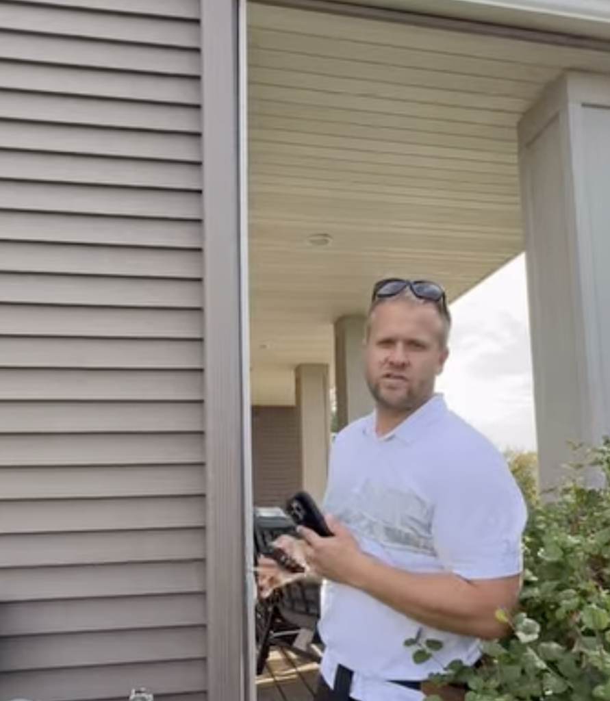 Noah Bergland stands at a house doorway with phone and keys, ready for roofing work post-storm, on behalf of Hook Agency.