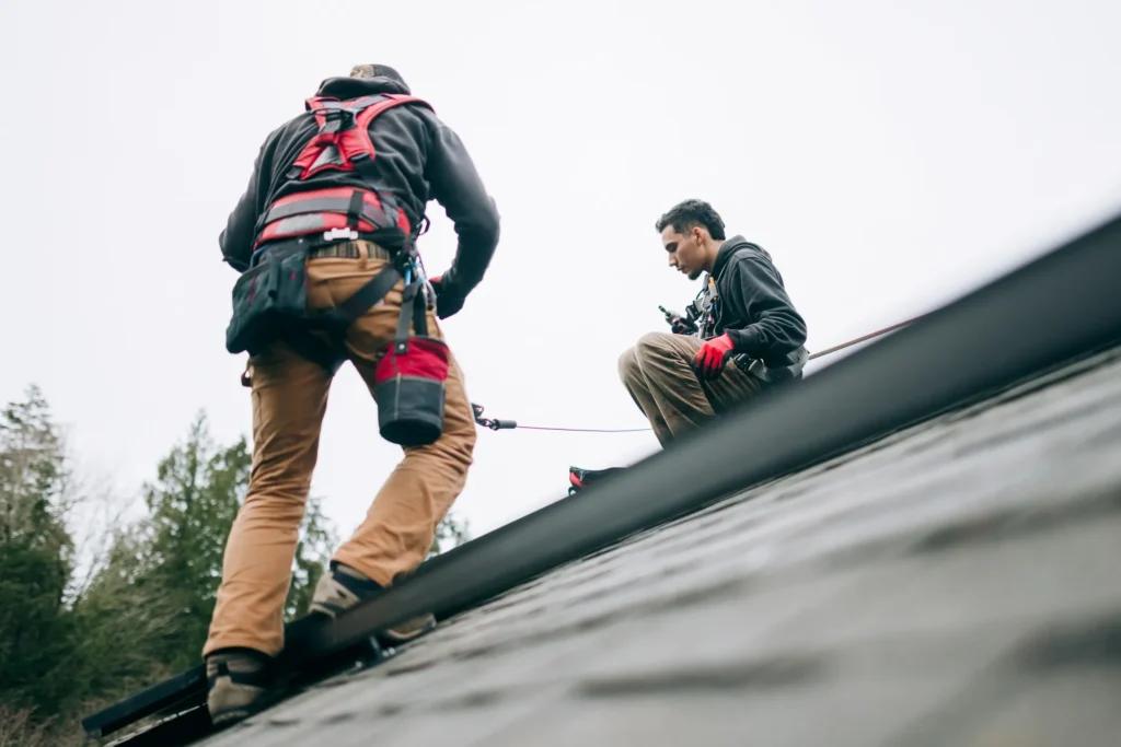 Noah Bergland - Roofing professionals in full safety gear work on a sloped roof using harnesses and ropes, following industry best practices.