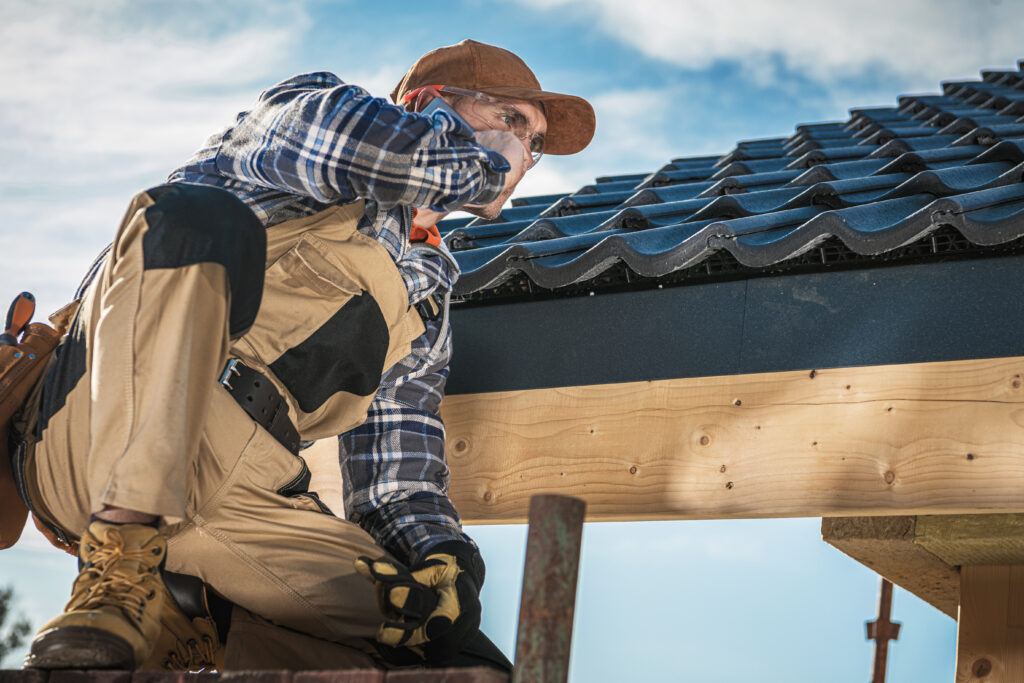 Construction worker in safety gear and plaid shirt inspects tiled roof from scaffolding—highlighting roofing tech advancements.