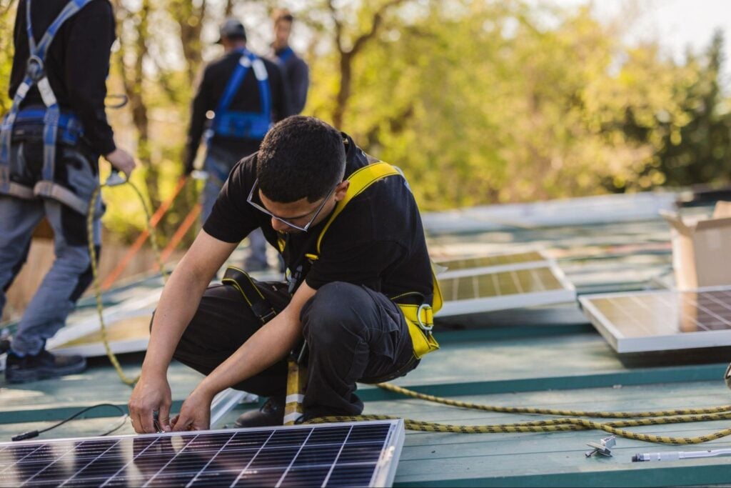 Roofing professional installs a solar panel with coworkers nearby, showcasing AI-driven innovation on site under clear, sunny skies.