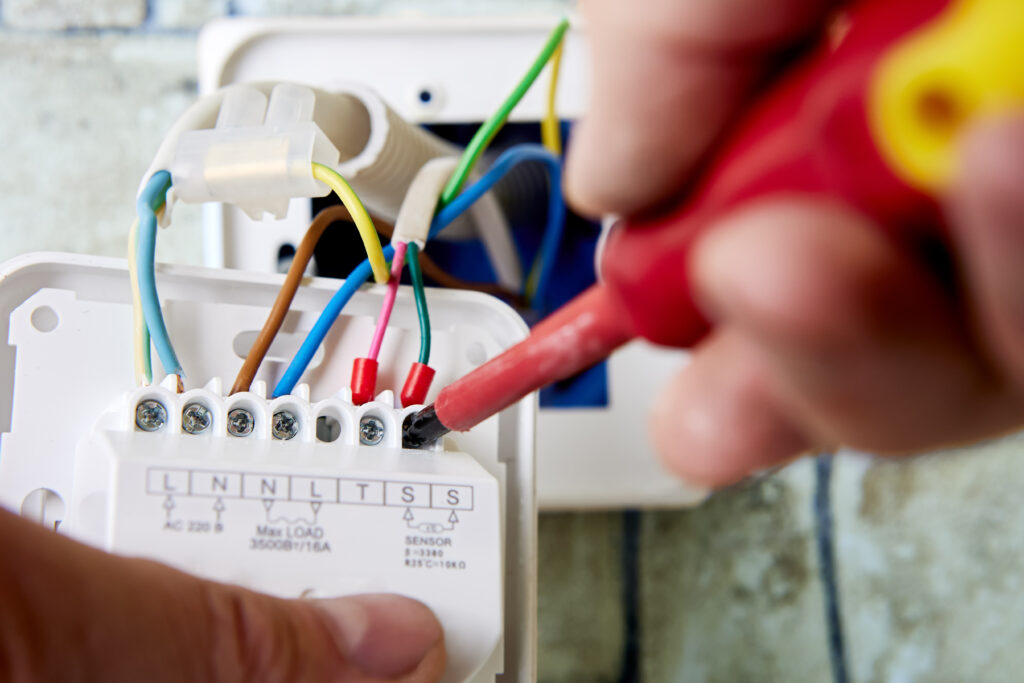 Technician secures colored wires inside a wall device with a screwdriver—key for maximizing profitable HVAC upsell opportunities.