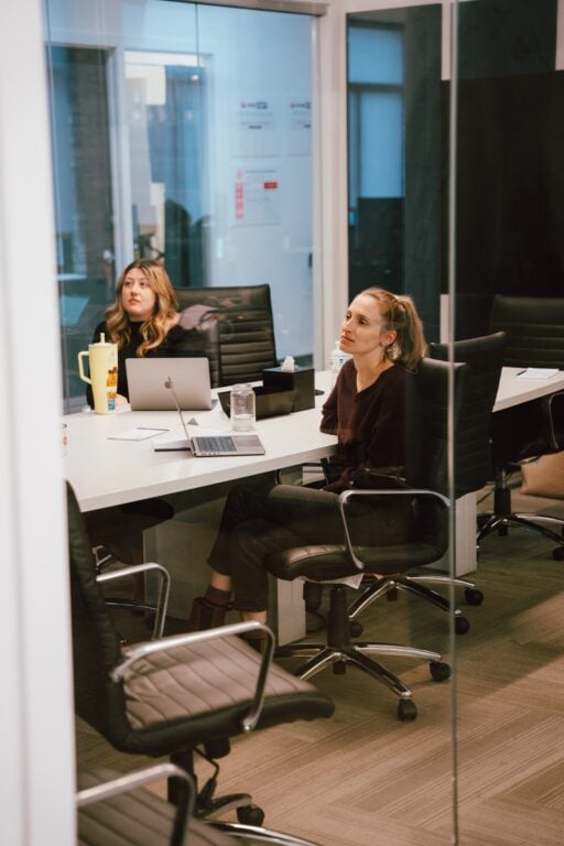 Two women discuss HVAC LSA management at a conference table in Hook Agency’s office, surrounded by laptops and glass walls.