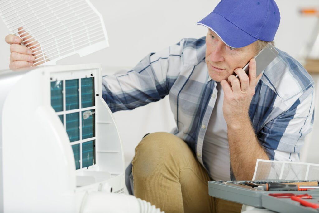 Home service technician inspects AC unit, tools nearby, communicating by phone—demonstrating trust through skill and responsiveness.