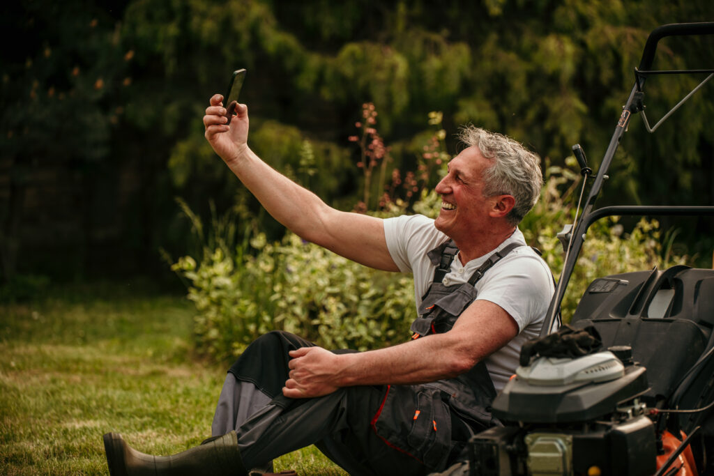 Home service professional in overalls takes a selfie by a lawn mower on grass, showcasing trust for your business's social media.
