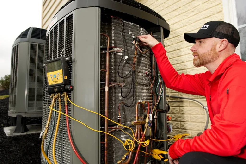HVAC technician in red jacket inspects outdoor unit at brick home, demonstrating expert service with tools and diagnostic equipment.