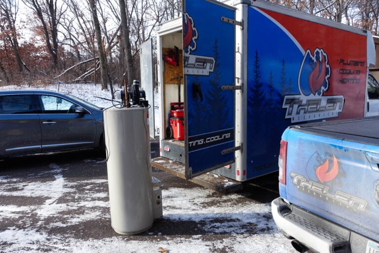 Water heater near "Thielen Heating" truck and trailer; efficient HVAC van setup shown in a snowy, tree-lined parking lot.