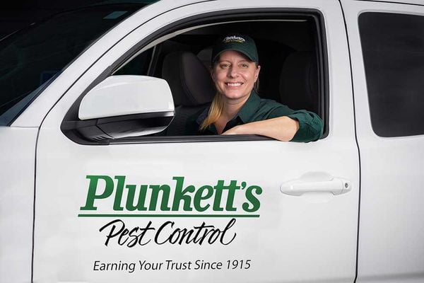 Plunkett’s Pest Control technician in green uniform sits in branded white vehicle, highlighting trusted pest control service.
