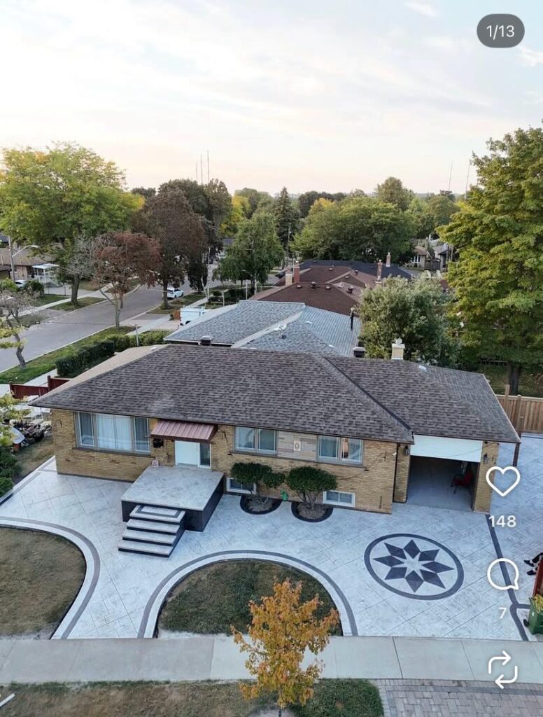 Aerial view of a prominent single-story brick house with patterned concrete drive, front potted shrubs, and surrounding trees.