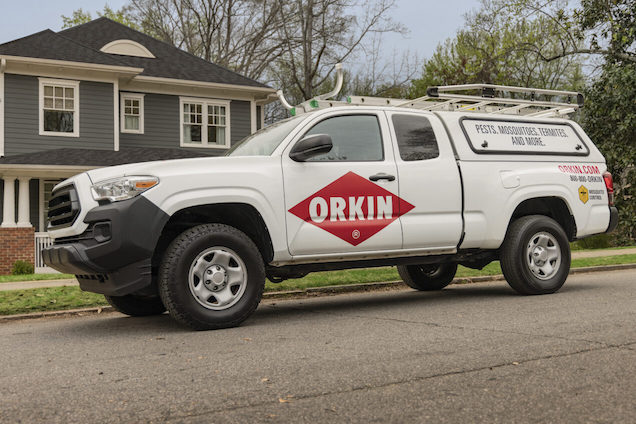 A branded white Orkin pest control truck with ladders is parked outside a gray suburban home, ready for expert service.