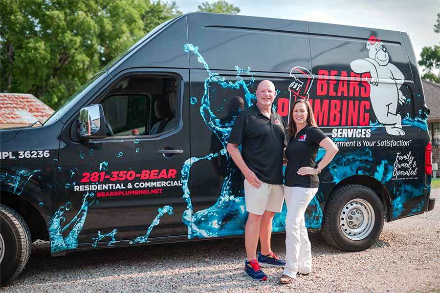 Man and woman confidently stand before a Bears Plumbing van, featuring water graphics and bear mascot—real contractors, not stock photos.