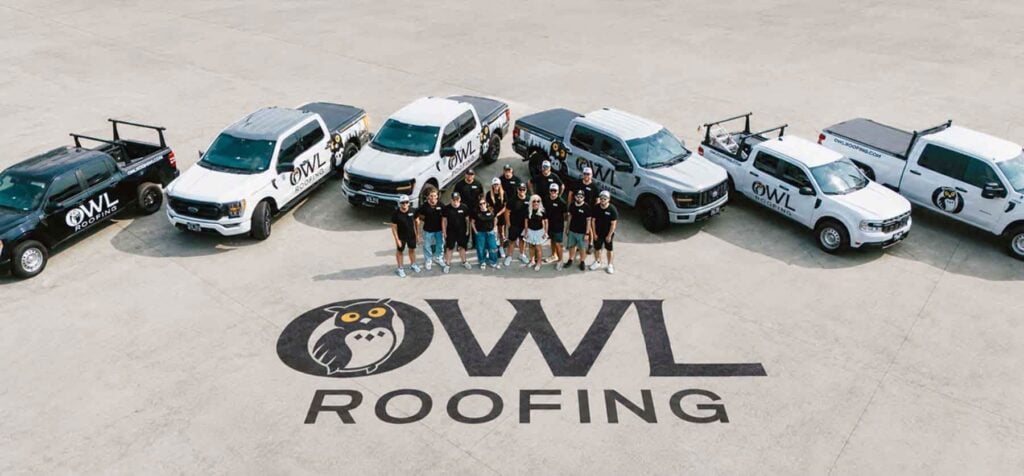 Team members stand before multiple Owl Roofing trucks on a concrete lot, with the prominent Owl Roofing logo painted on the ground, highlighting brand presence—showcasing successful branding in partnership with Hook Agency.